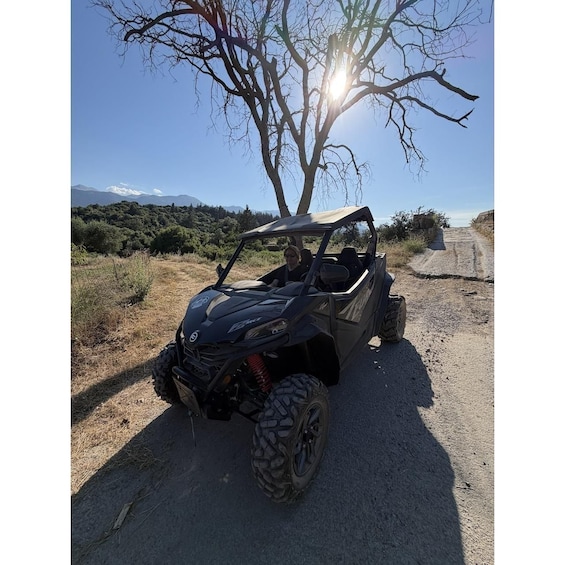 A black off-road vehicle parked on a dirt road with a tree and mountains in the background. 3