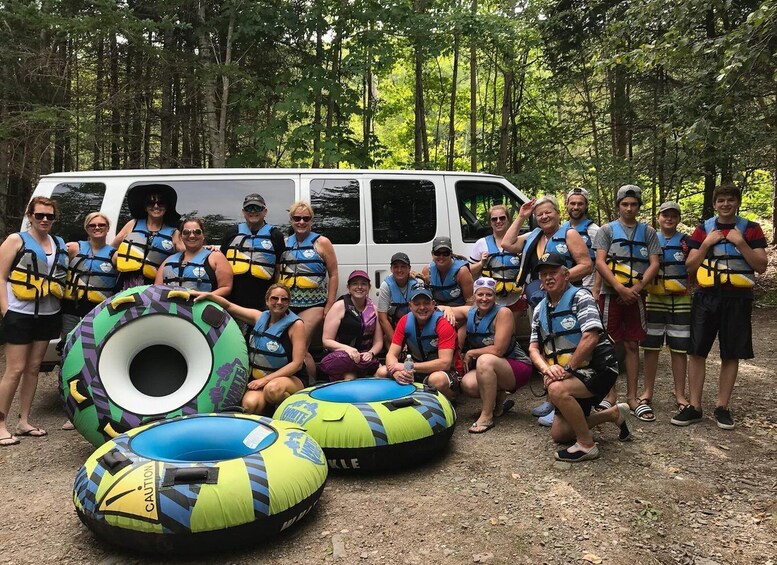 A group of people in life jackets posing with inflatable rings and a van in a forest. 4