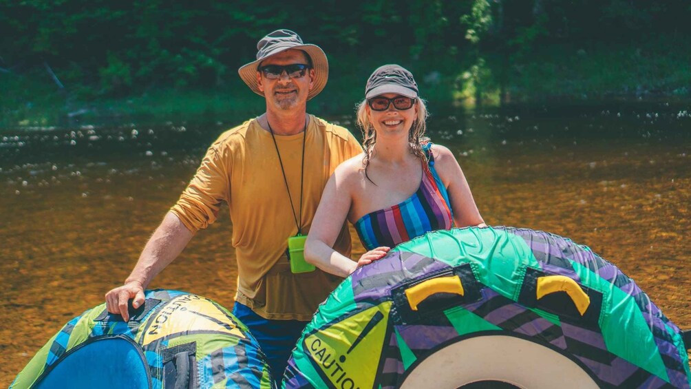 A man and a woman standing by a body of water, holding a large inflatable raft. 3