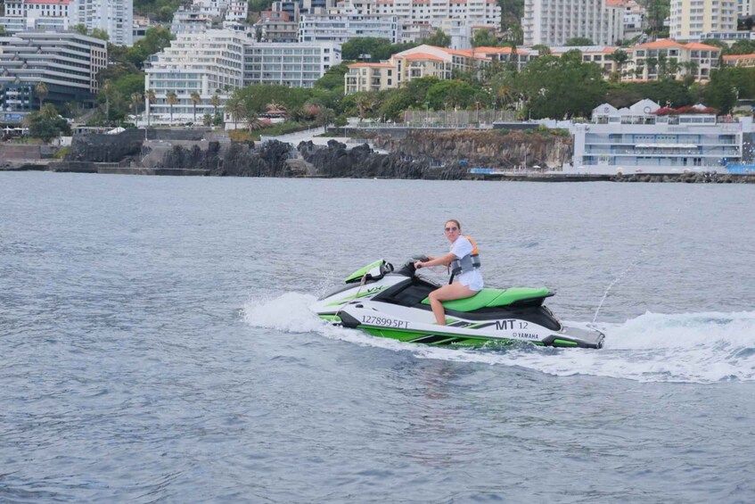 A person riding a green and white Yamaha jet ski on a body of water with buildings in the background. 4