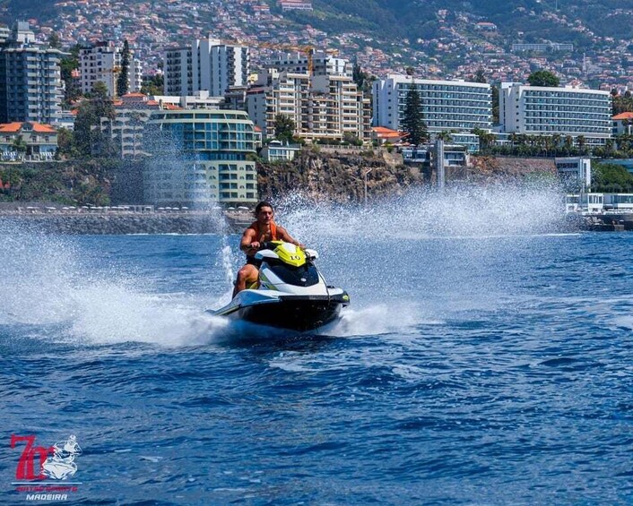 A person jet-skiing on a body of water with a cityscape in the background. 1