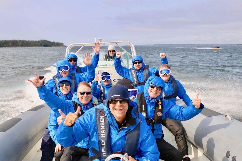 A group of people on a boat wearing blue jackets and life vests, with a boat in the background. 1
