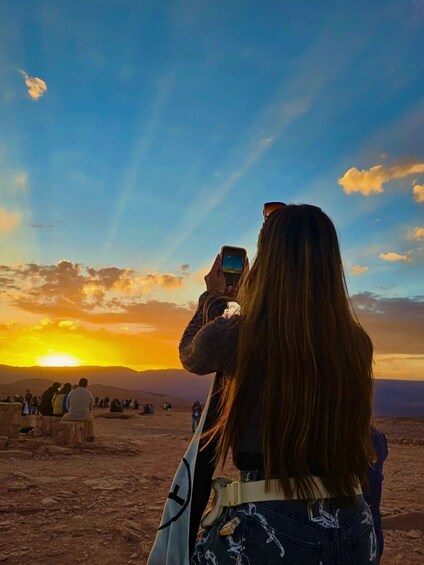 A person taking a photo of a sunset with a crowd in the background. 2
