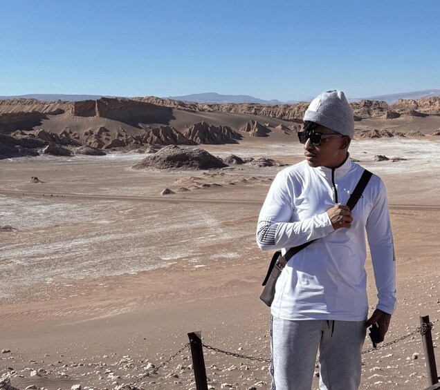 A person standing on a sandy terrain with rocky formations in the background. 4