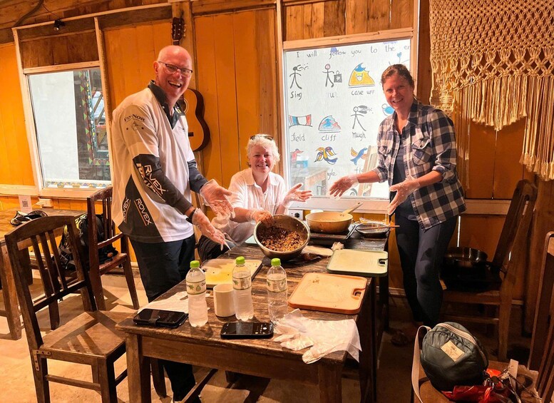 Three people cooking in a rustic kitchen with wooden walls and a guitar in the background. 4