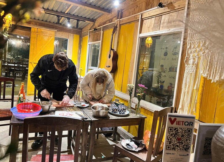 Two people preparing food at a wooden table with yellow walls, a guitar, and a sign with a QR code. 3