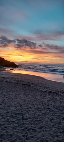 A beach at sunset with waves and a person walking. 4