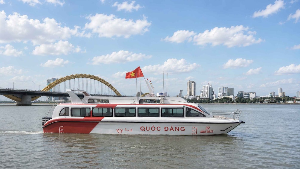 A boat with a flag, a bridge, and a city skyline in the background. 2