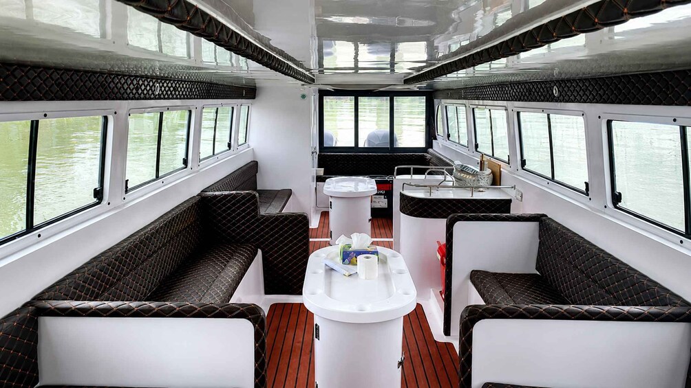 A boat's interior with cushioned seating, a central table with a bottle, and a windowed side. 3