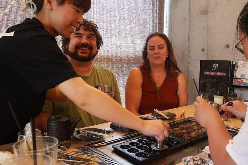 Une personne prépare des aliments sur un comptoir, avec un panneau affichant le menu en arrière-plan. 1