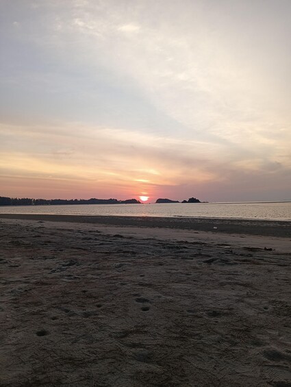 A beach at sunset with the sun near the horizon, calm water, and a distant shoreline. 2