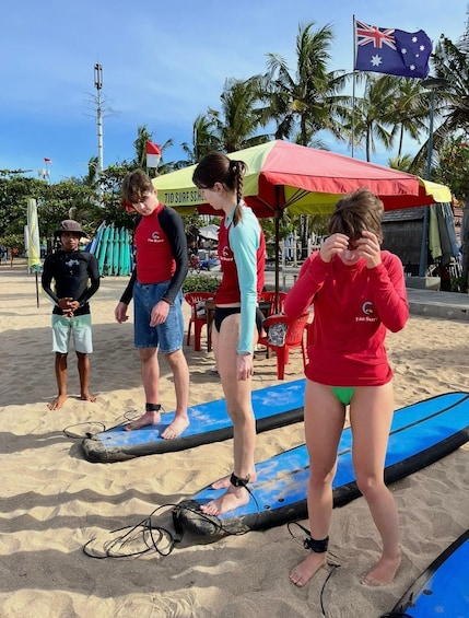 People on surfboards at a beach with palm trees and a flag in the background. 3