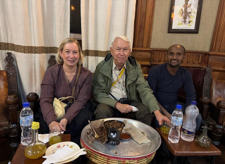 Three people seated at a table with a traditional meal, including a metal plate with food and drinks. 2