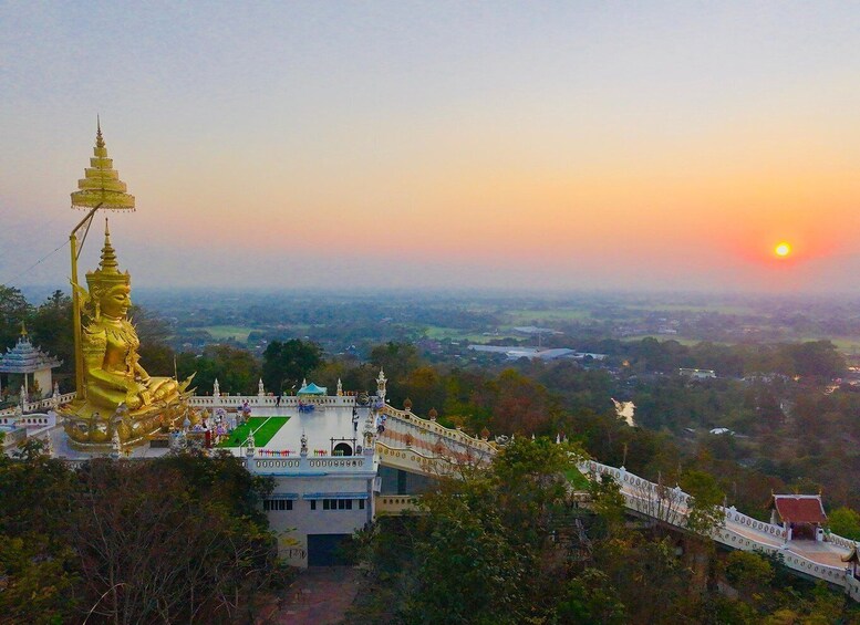 Een gouden Boeddhabeeld bij zonsondergang, met een tempelcomplex op de achtergrond. 5