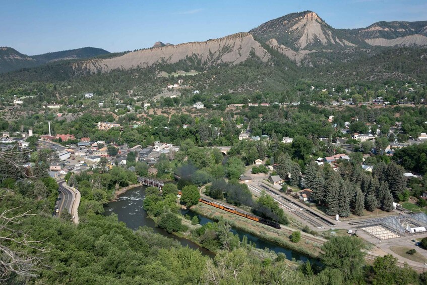 A train traveling through a town surrounded by mountains and greenery. 5