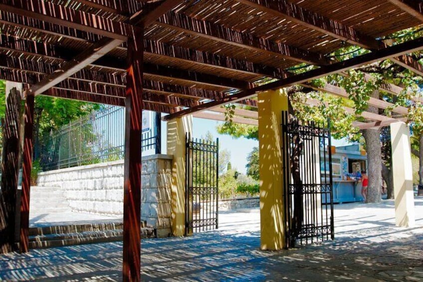 Un espacio al aire libre cubierto con una pérgola, escalones de piedra, un portón metálico y un edificio al fondo. 1