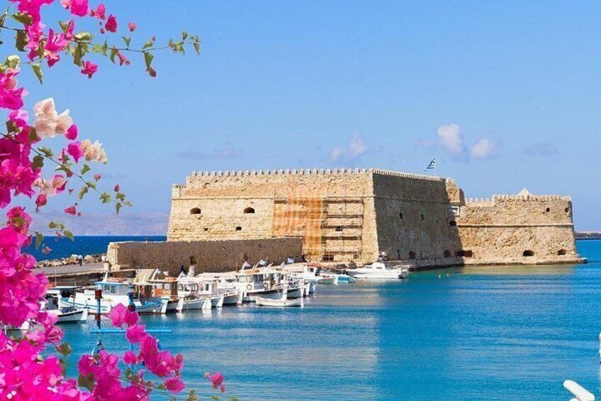 A historic stone fortification by the sea with boats docked in the foreground. 1