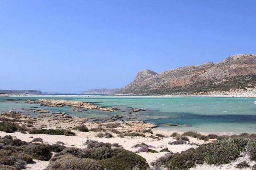 A coastal landscape with rocky terrain, clear blue waters, and sparse vegetation. 2