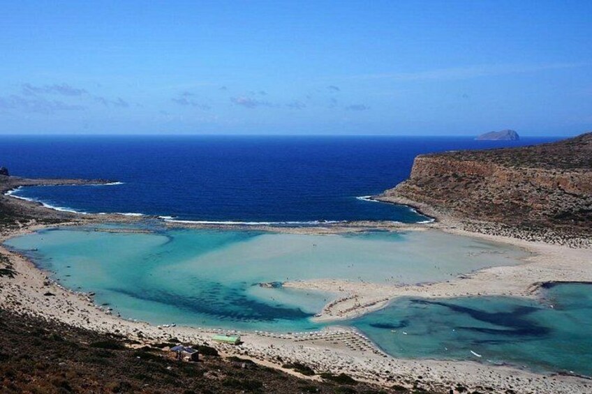 Een kustlandschap met een heldere blauwe zee, een zandstrand en een rotsachtige landtong. 1