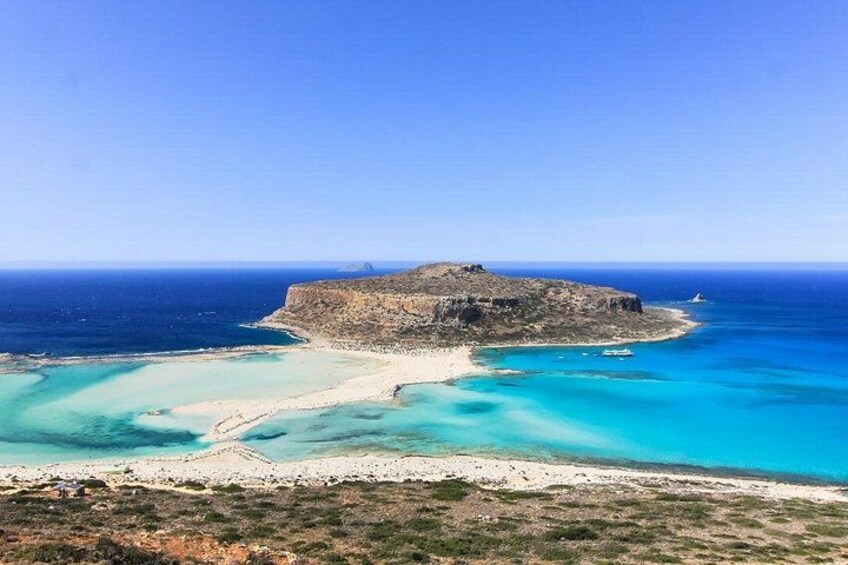 A coastal landscape with a prominent rocky island, clear turquoise waters, and a sandy beach. 3
