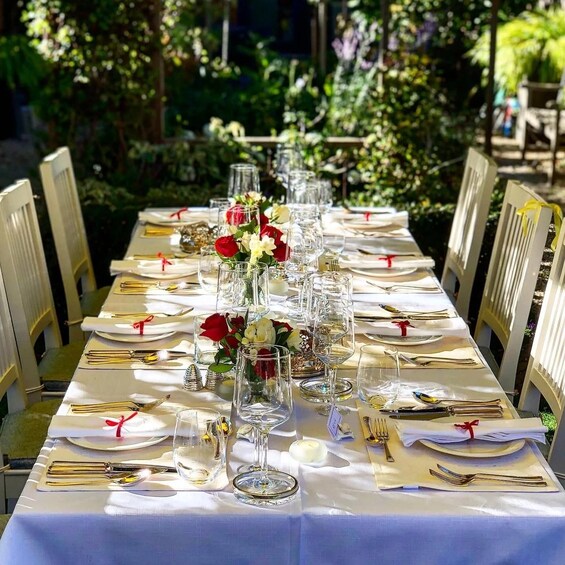 A table set for a formal outdoor dining event with white tablecloths, glassware, and red roses. 2