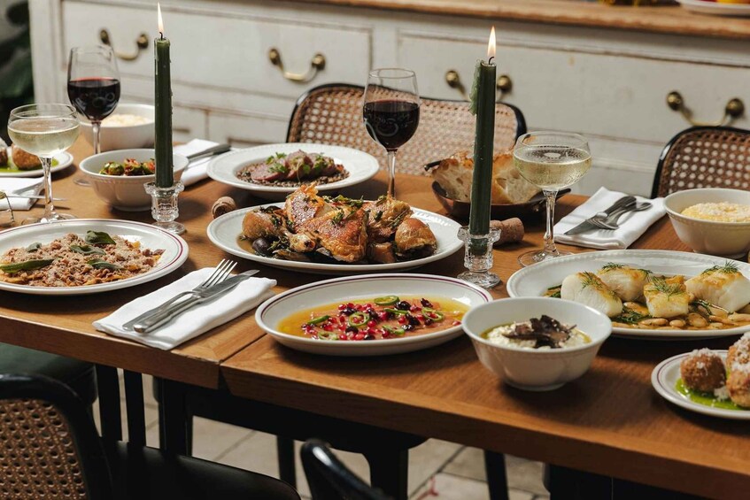 A wooden dining table with various dishes, glasses of wine, and candles. 1