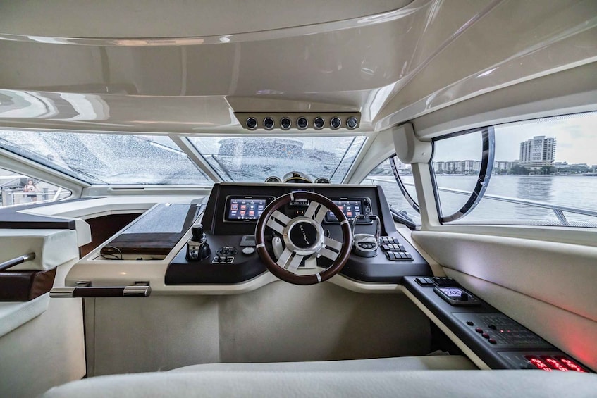 The interior of a boat with a steering wheel, control panel, and windows overlooking a body of water. 1