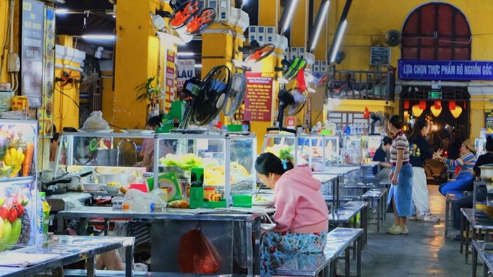 A bustling indoor market with various stalls selling fruits, vegetables, and other goods. 5
