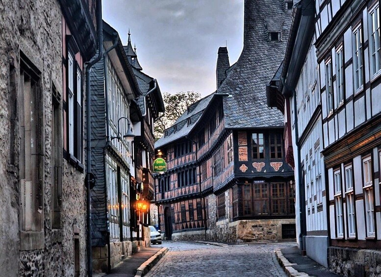 A narrow cobblestone street lined with historic half-timbered buildings, a sign for a pub, and a church steeple. 2