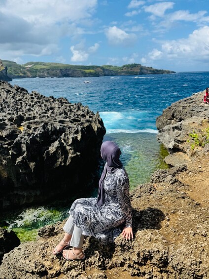 A person sitting on a rocky cliff overlooking a blue ocean. 5