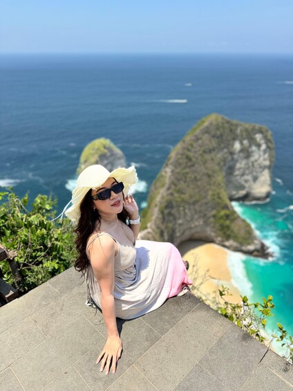 A person sitting on a stone ledge overlooking a coastal landscape with cliffs and turquoise waters. 3