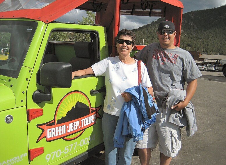 Dos personas de pie al lado de un Jeep verde con un logo y texto en la carrocería. 2