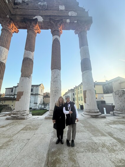 Two people standing under ancient stone columns with a fire burning above. 2