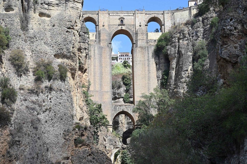 A stone aqueduct with three arches, surrounded by rocky terrain and sparse vegetation. 5