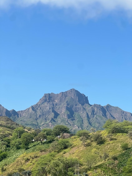 A mountain range with lush greenery in the foreground and a clear blue sky. 2