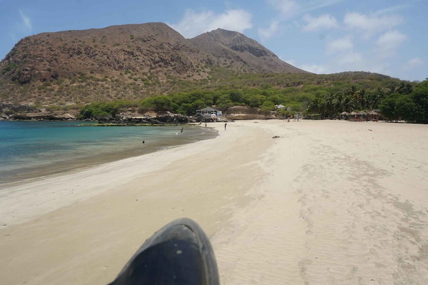 A beach with clear turquoise water, sandy shore, and a mountain in the background. 1