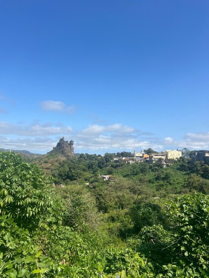 A landscape with a prominent rock formation, dense greenery, and scattered buildings. 3