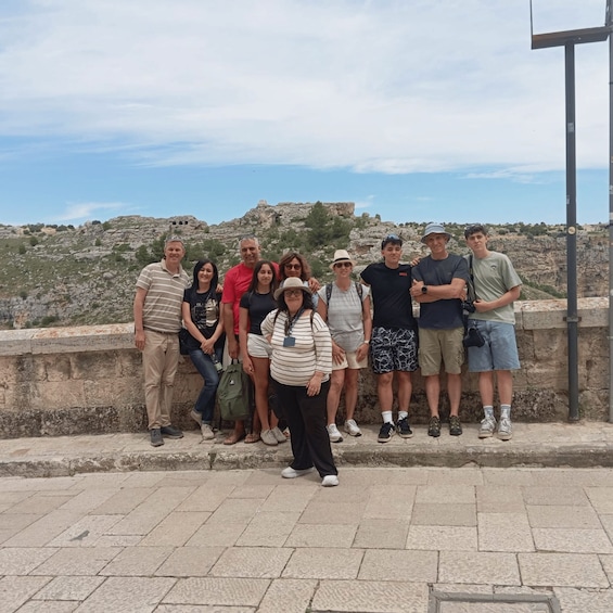 A group of people standing on a stone platform with a rocky landscape and ruins in the background. 2