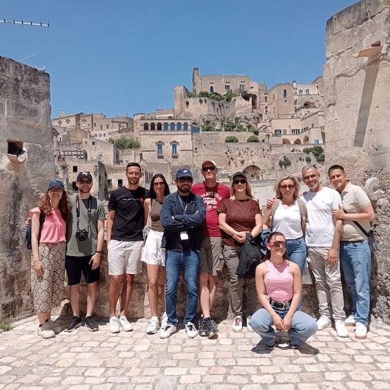 A group of people posing in front of historic stone buildings with a clear blue sky. 3