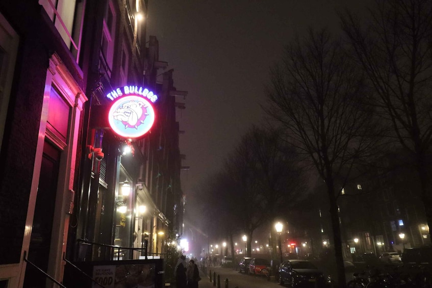 Yökuva kadusta, jossa näkyy neonvalomainos ravintolalle nimeltä ”The Bull Dog”, katuvaloja, parkkeerattuja autoja ja lehdettömiä puita. 3