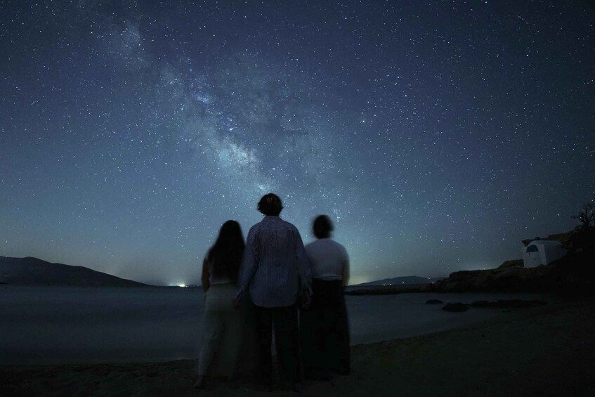Three people standing on a beach under a starry night sky. 1