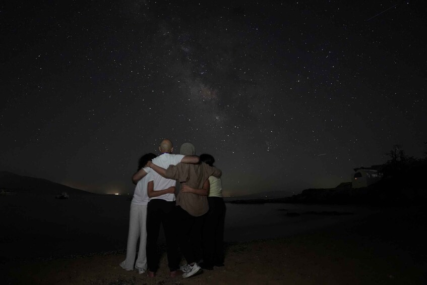 A group of people standing on a beach under a starry night sky. 4