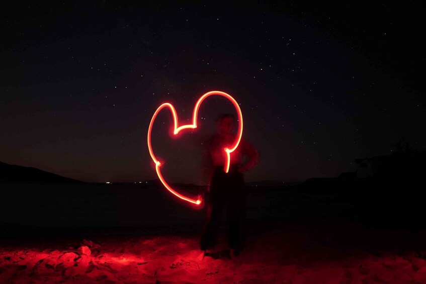 A person creating a heart shape with red light on a dark desert landscape. 2