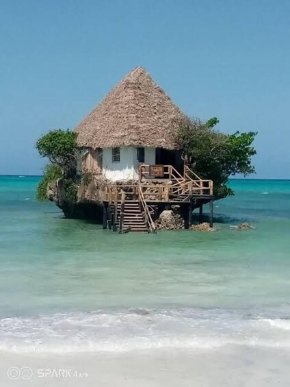 A thatched-roof house on stilts over clear turquoise water. 4