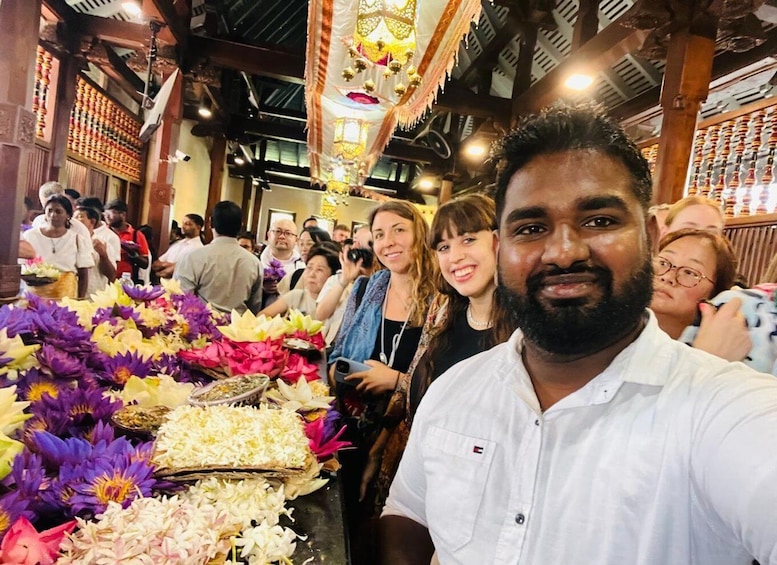 A group of people in a traditional setting with a table of flowers and food. 1