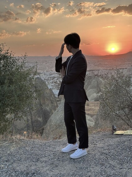 A person in a suit and white shoes standing on a rocky terrain with a sunset in the background. 5