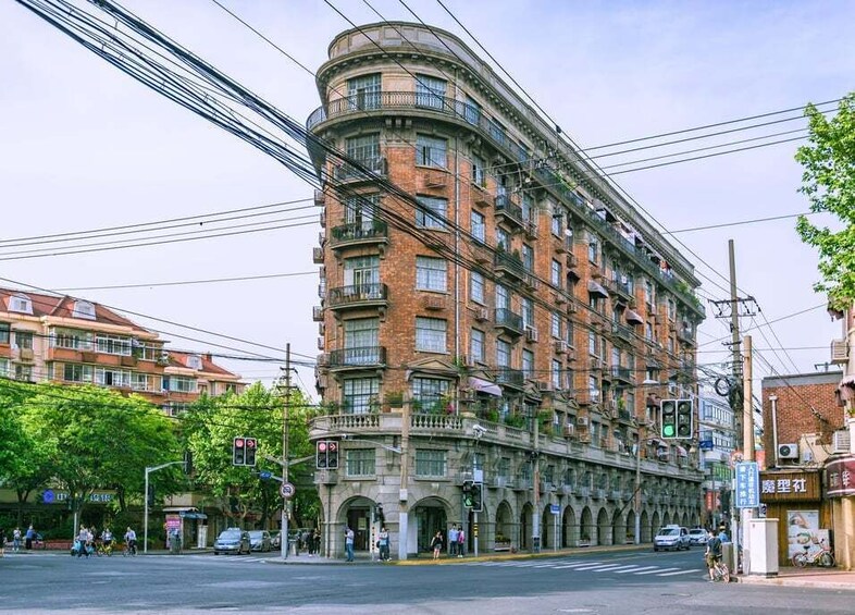 A curved brick building with multiple balconies and windows, located at a street intersection with traffic lights and pedestrians. 5