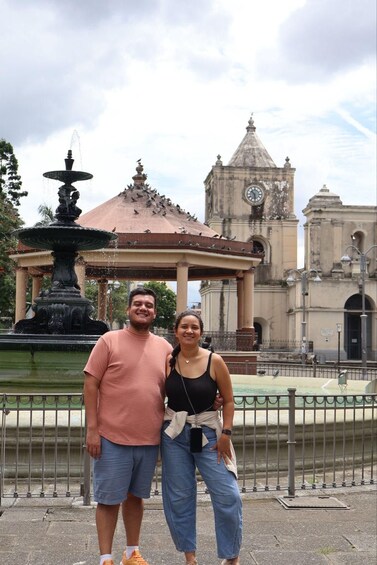 A couple standing in front of a fountain with a clock tower in the background. 3