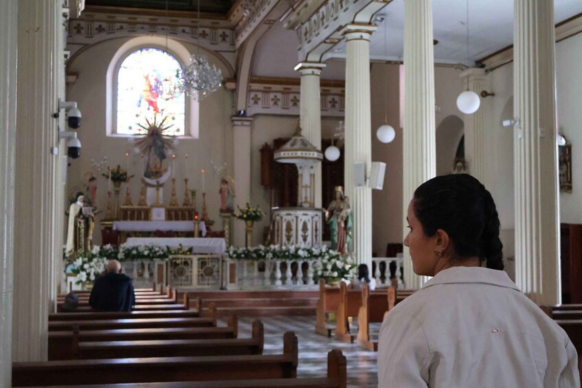 An interior of a church with rows of pews, a central altar, and a large stained glass window. 5