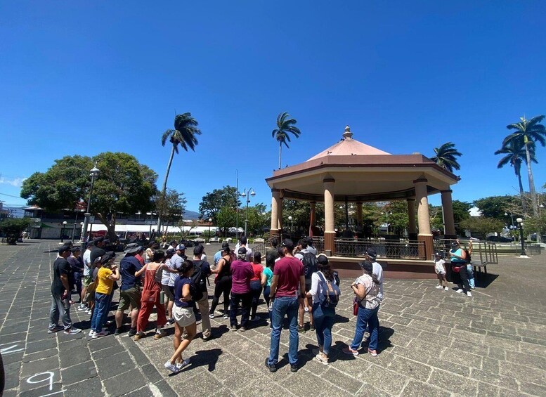 A group of people gathered around a gazebo in a public square with palm trees in the background. 3